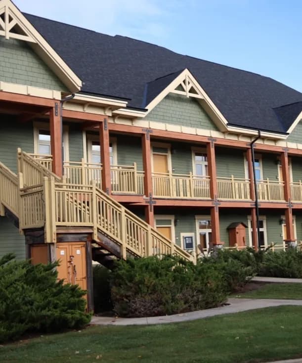 A lodge building at Hilton Grand Vacations Club Blue Mountain Canada with sage green siding, timber balconies, and stairs finished in warm wood tones.