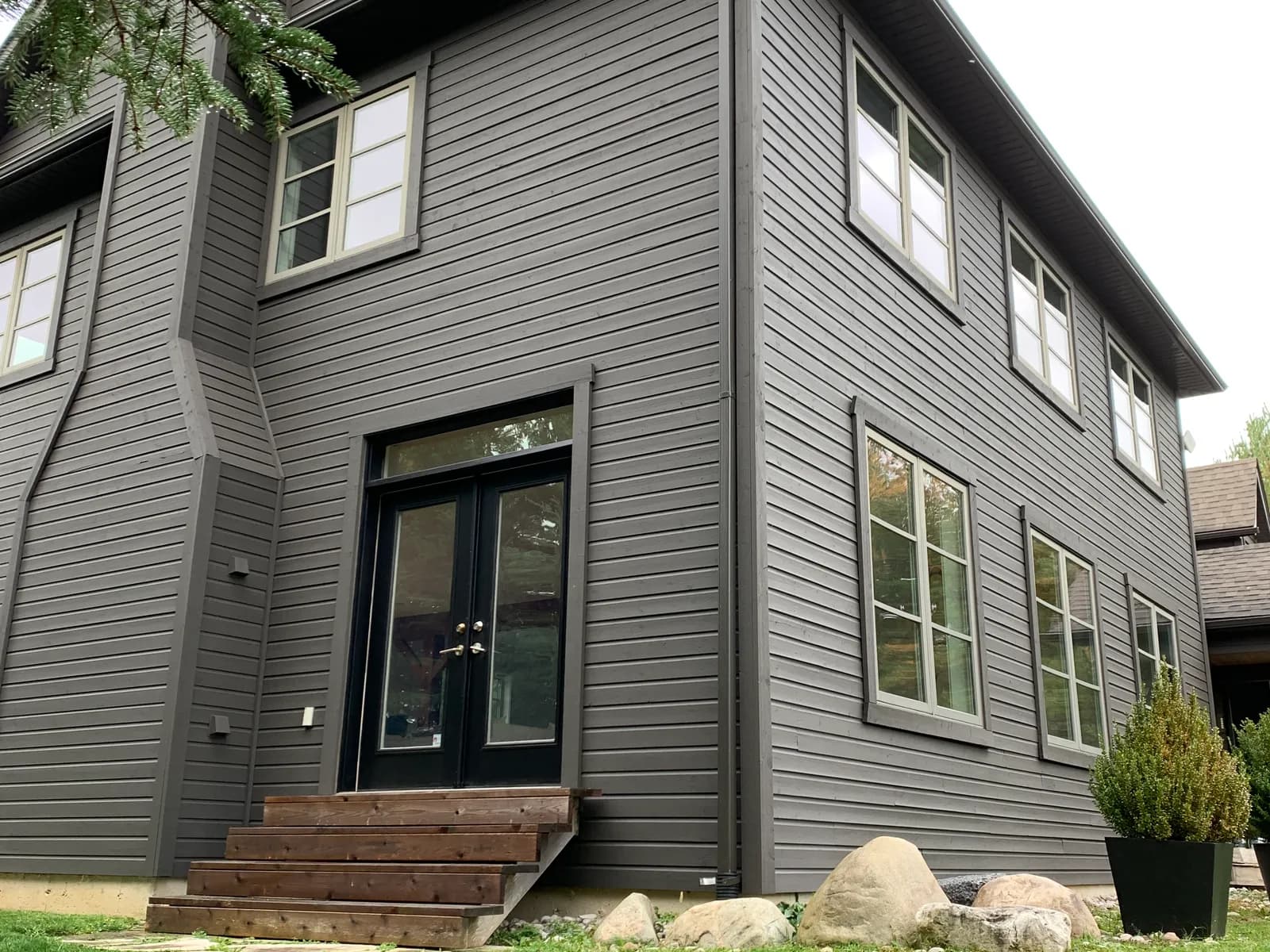 A Clarksburg home finished in deep charcoal grey, its board siding, trim and window frames all repainted, with a cedar step up to the patio doors.
