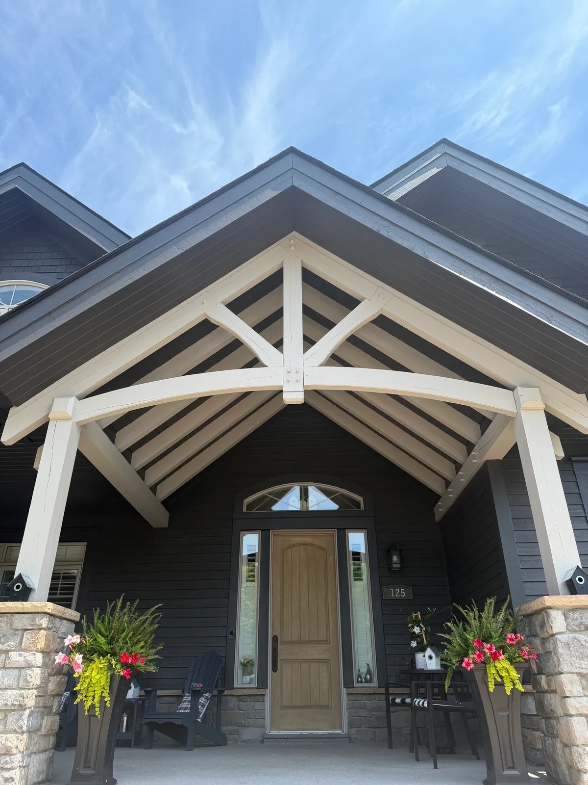 The timber frame gable entry of a Thornbury home, its heavy trusses picked out in white against the deep charcoal siding above a wood front door.